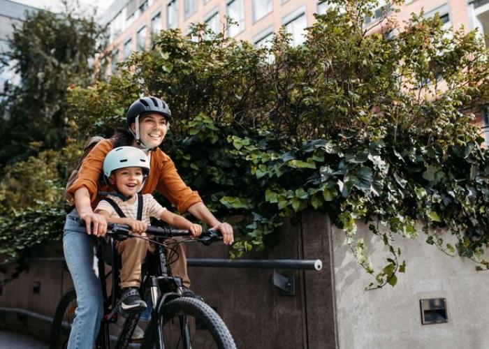 Enfant casqué faisant du vélo avec sa maman, sur un porte enfant en position avant
