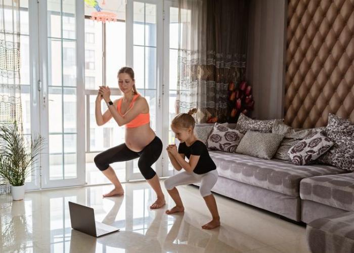 Femme enceinte fait du sport avec sa fille devant un ordinateur