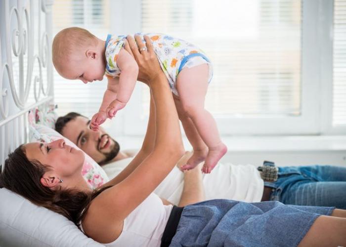 Maman, portant son bébé, allongée sur un lit avec son mari
