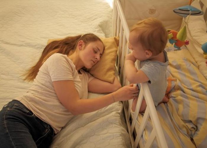 Maman dormant à côté de son bébé qui se trouve dans lit à barreau