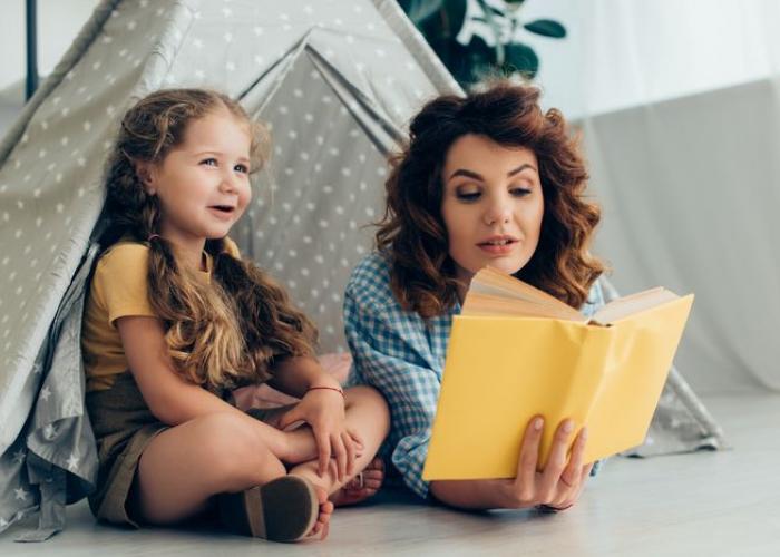 Babysitter lisant un livre à une petite fille sous une cabane tente