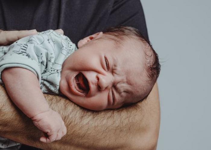 Bébé pleurant dans les bras de son papa qui tente de le calmer