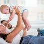 Maman, portant son bébé, allongée sur un lit avec son mari