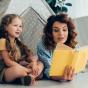 Babysitter lisant un livre à une petite fille sous une cabane tente