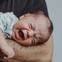 Bébé pleurant dans les bras de son papa qui tente de le calmer