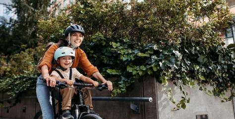 Enfant casqué faisant du vélo avec sa maman, sur un porte enfant en position avant