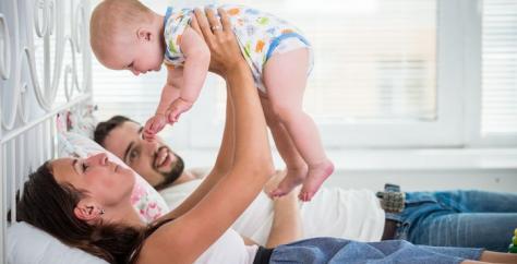 Maman, portant son bébé, allongée sur un lit avec son mari