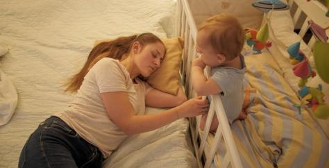 Maman dormant à côté de son bébé qui se trouve dans lit à barreau