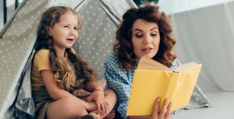 Babysitter lisant un livre à une petite fille sous une cabane tente