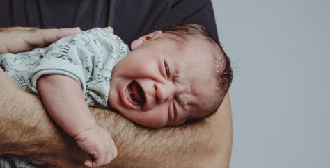 Bébé pleurant dans les bras de son papa qui tente de le calmer