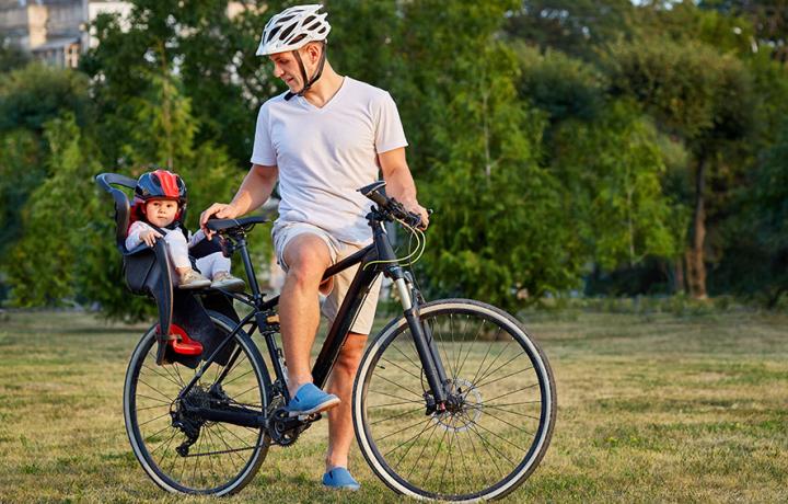 Enfant sur porte bébé à l'arrière d'un vélo avec son papa